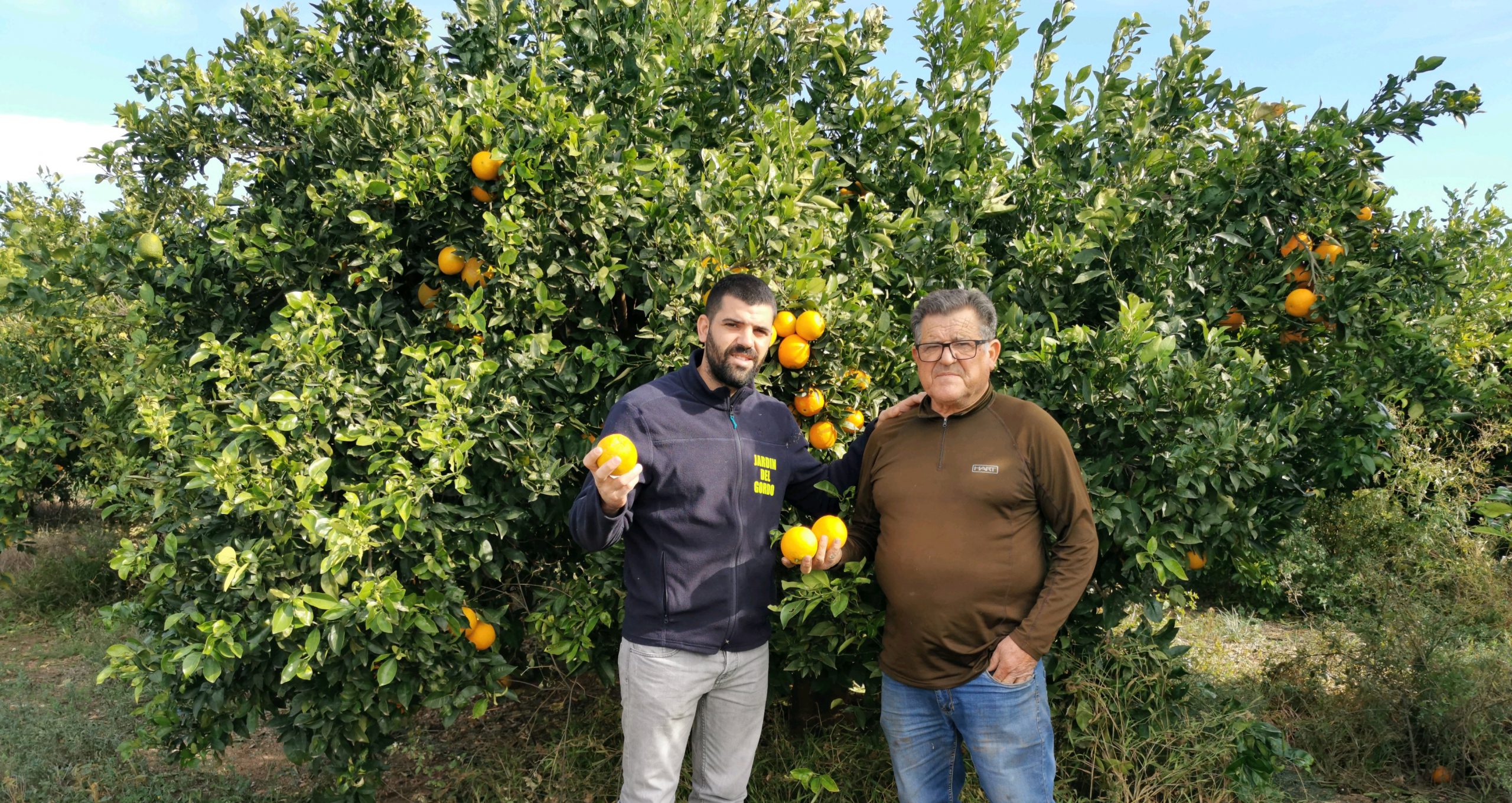 Farmer Sergio Muñoz and his father posing in front of his orange farm