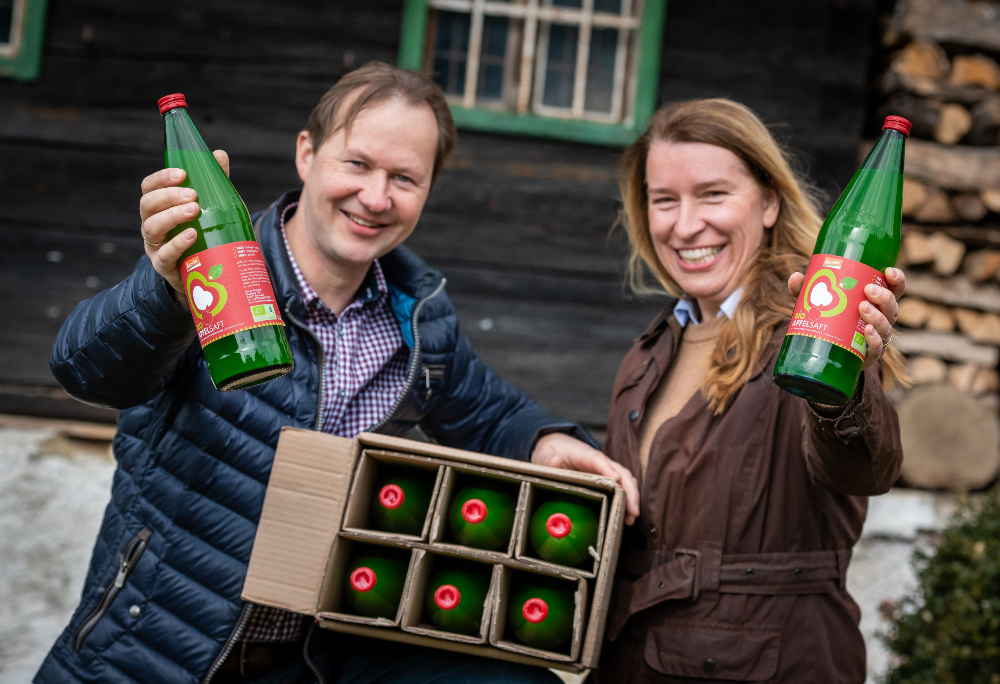 Two farmers with a bottle of apple juice in hand and box of bottles of apple juice